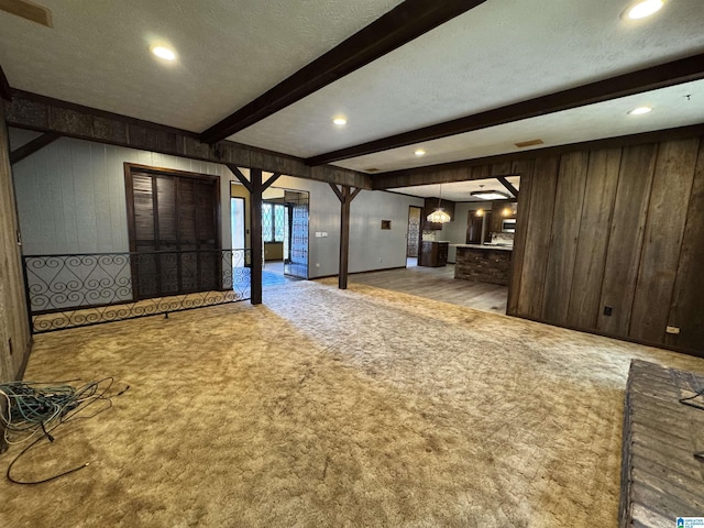 unfurnished living room with carpet floors, wood walls, beamed ceiling, and a textured ceiling