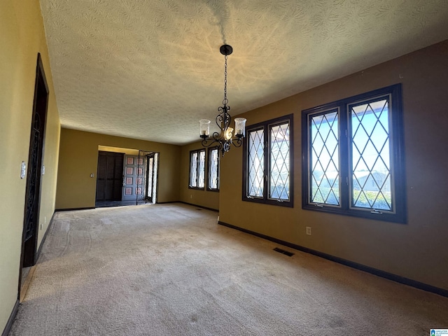 carpeted spare room featuring a chandelier, a textured ceiling, visible vents, and baseboards