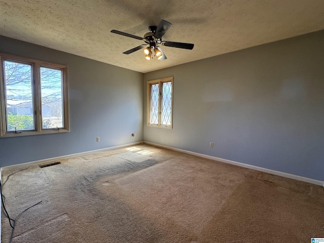 empty room featuring a textured ceiling, ceiling fan, carpet floors, visible vents, and baseboards