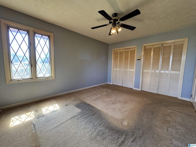 unfurnished bedroom with baseboards, ceiling fan, a textured ceiling, carpet floors, and two closets