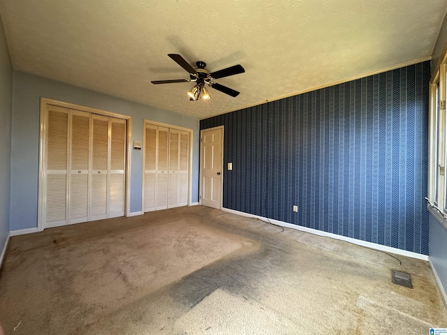 unfurnished bedroom with wallpapered walls, visible vents, baseboards, a textured ceiling, and multiple closets