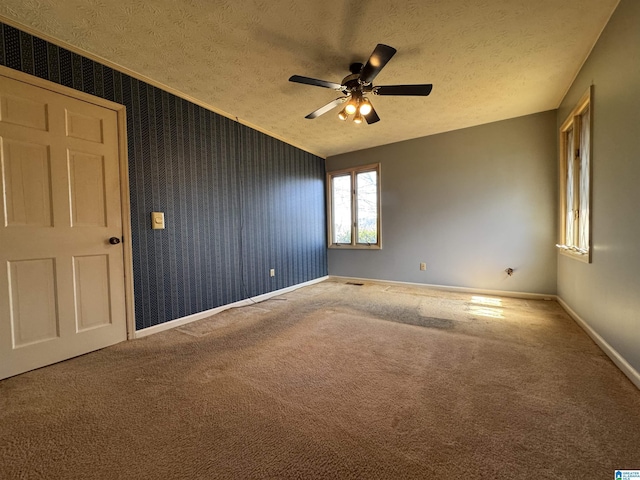 carpeted spare room with a textured ceiling, wallpapered walls, a ceiling fan, and baseboards