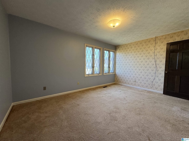 empty room featuring carpet, visible vents, a textured ceiling, baseboards, and wallpapered walls