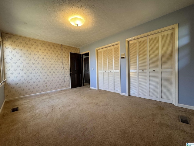 unfurnished bedroom with a textured ceiling, carpet, two closets, and visible vents