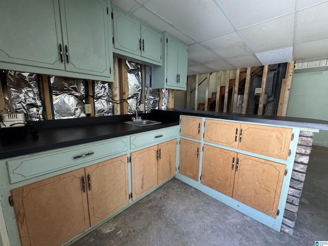 kitchen featuring concrete flooring, a peninsula, a drop ceiling, and a sink