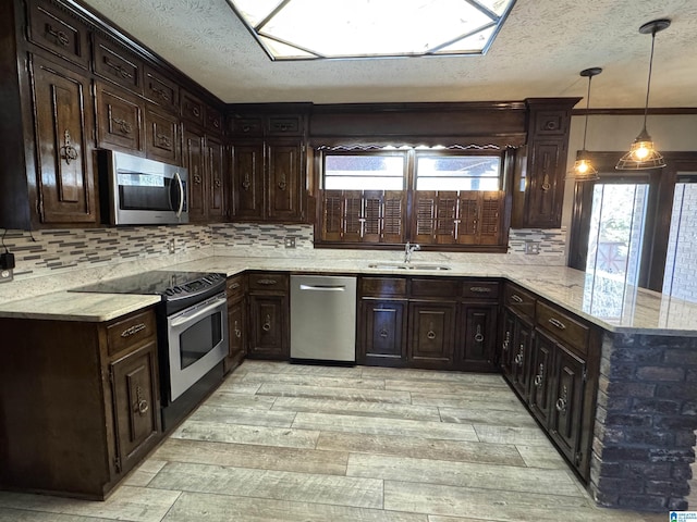 kitchen featuring a peninsula, light stone countertops, appliances with stainless steel finishes, and a sink