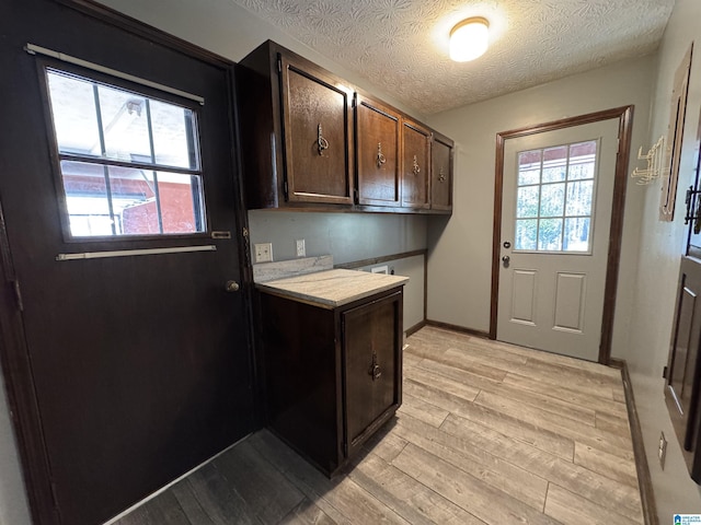 laundry room with a textured ceiling, hookup for a washing machine, baseboards, light wood-type flooring, and cabinet space