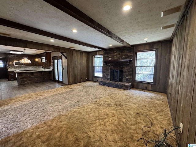 unfurnished living room with a textured ceiling, wooden walls, carpet floors, a fireplace, and beamed ceiling