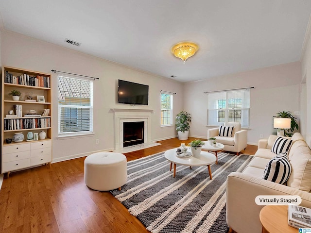 living area with a fireplace with raised hearth, wood finished floors, visible vents, and baseboards