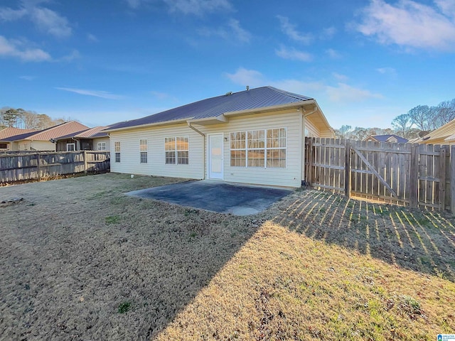 back of property with fence, metal roof, a lawn, and a patio