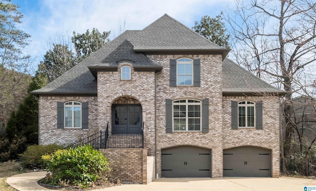 french country style house featuring a shingled roof, brick siding, driveway, and an attached garage