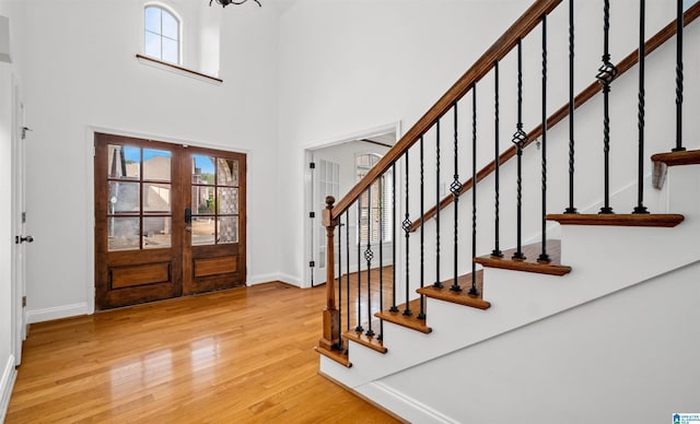 entryway featuring french doors, stairway, a towering ceiling, light wood-style floors, and baseboards