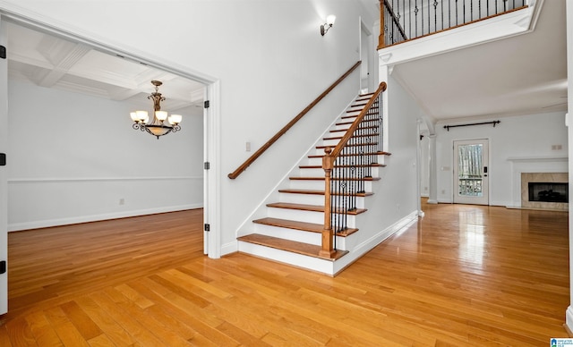 stairway featuring a fireplace, coffered ceiling, baseboards, hardwood / wood-style floors, and an inviting chandelier