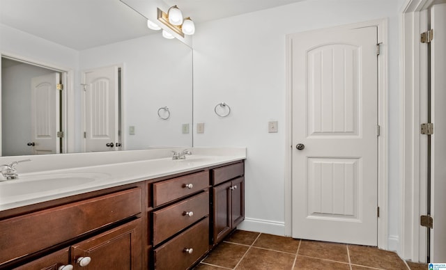 full bath featuring baseboards, double vanity, a sink, and tile patterned floors