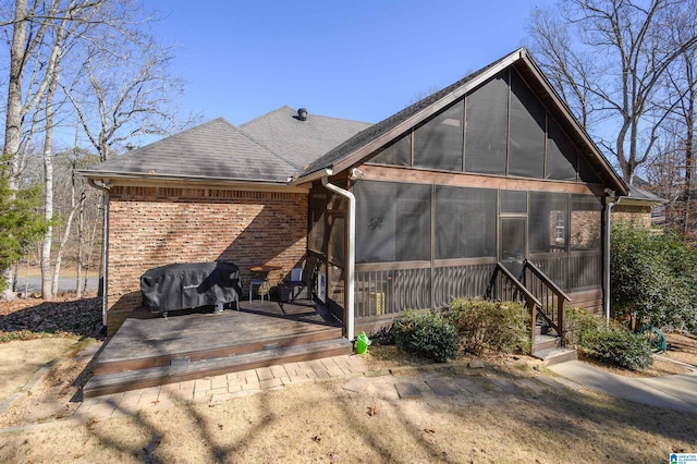 back of property with a sunroom, roof with shingles, and brick siding