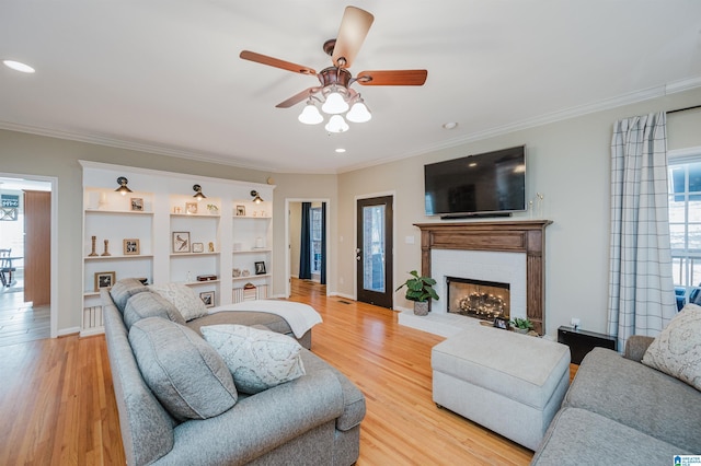 living area featuring recessed lighting, a fireplace, baseboards, light wood finished floors, and crown molding