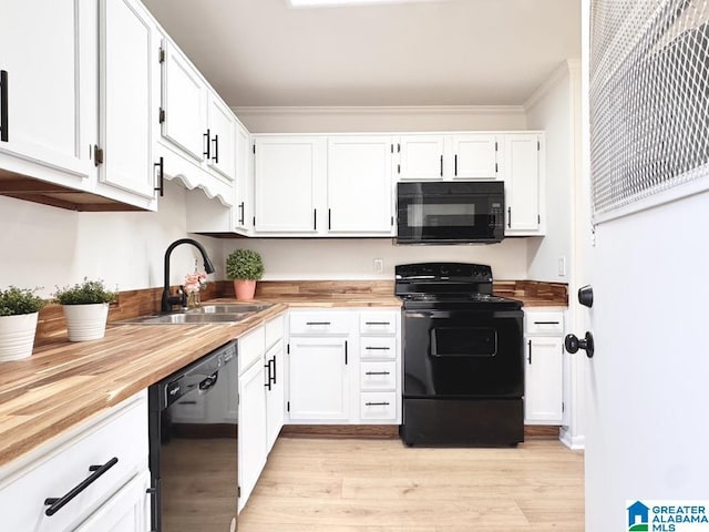 kitchen featuring butcher block countertops, a sink, white cabinets, light wood-type flooring, and black appliances