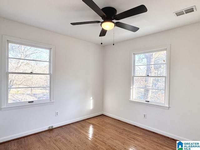 empty room with ceiling fan, wood finished floors, visible vents, and baseboards