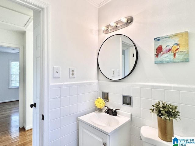 half bathroom with toilet, a wainscoted wall, wood finished floors, vanity, and tile walls