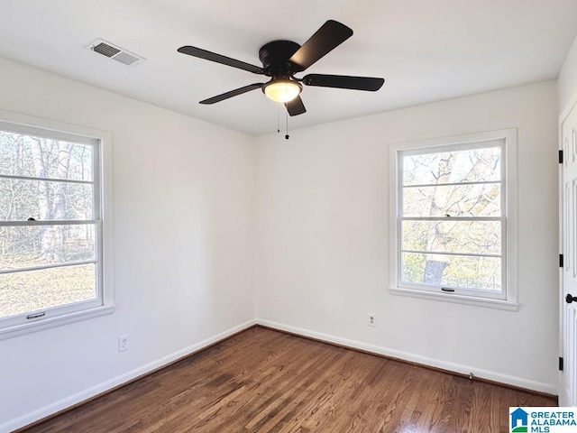 empty room featuring plenty of natural light, wood finished floors, visible vents, and baseboards