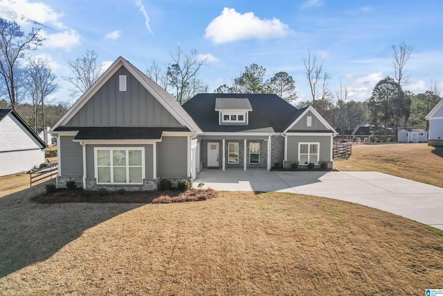 craftsman house featuring stone siding, fence, a front lawn, and board and batten siding