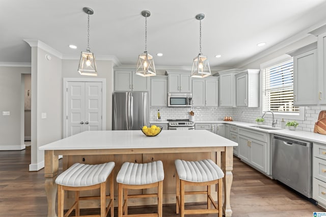 kitchen with dark wood finished floors, crown molding, stainless steel appliances, a sink, and a kitchen breakfast bar