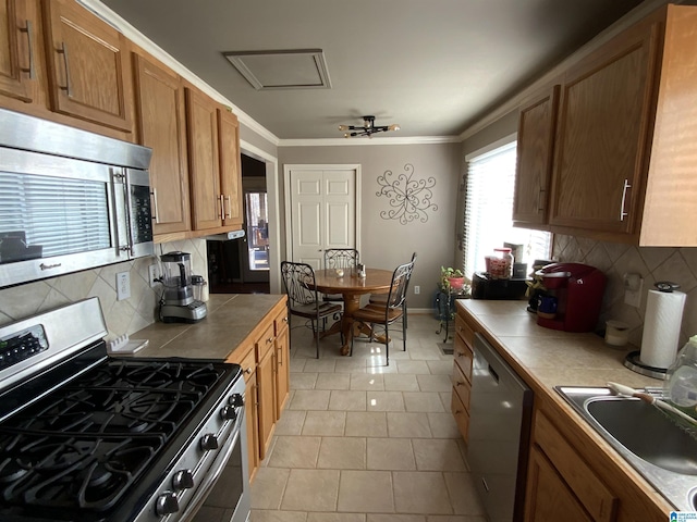 kitchen with stainless steel appliances, brown cabinetry, a sink, and tile countertops