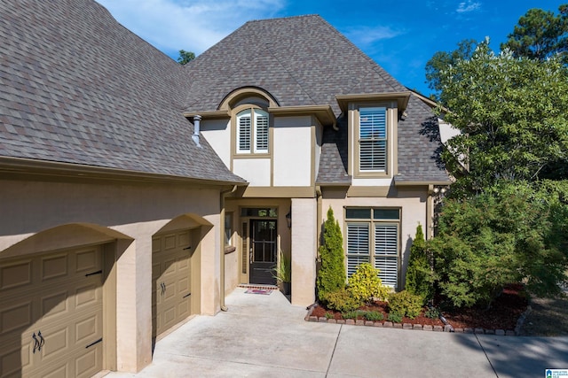 french provincial home featuring concrete driveway, roof with shingles, an attached garage, and stucco siding