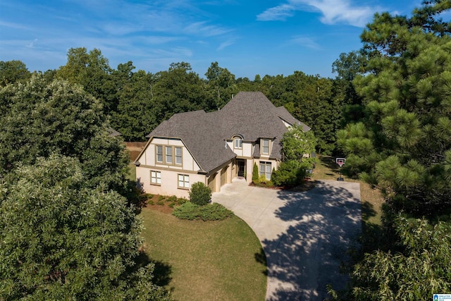 exterior space with driveway, a forest view, roof with shingles, and stucco siding