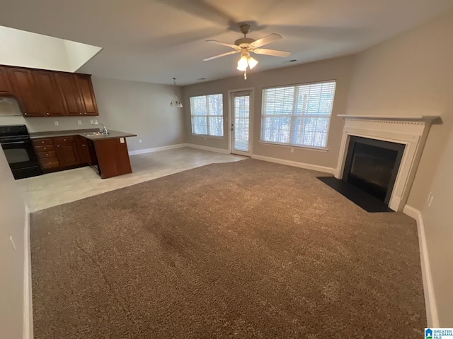 kitchen with baseboards, range, light colored carpet, a fireplace with flush hearth, and open floor plan