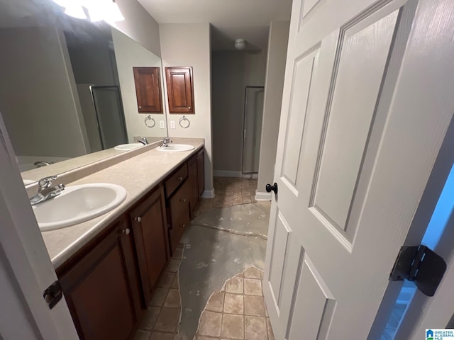 full bath with double vanity, a shower stall, baseboards, and a sink