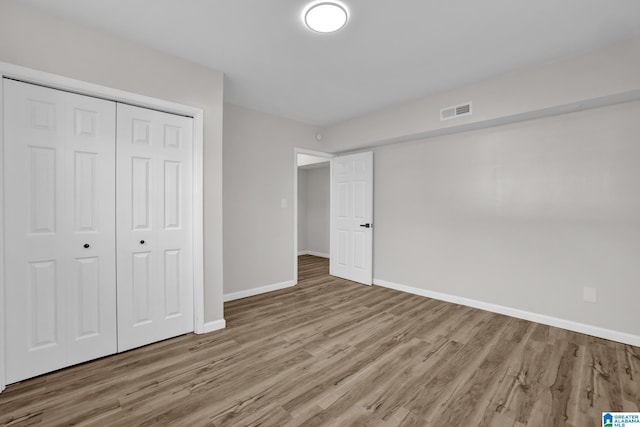 unfurnished bedroom featuring a closet, visible vents, baseboards, and wood finished floors