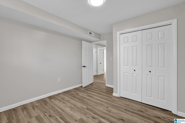 unfurnished bedroom featuring baseboards, a closet, visible vents, and wood finished floors