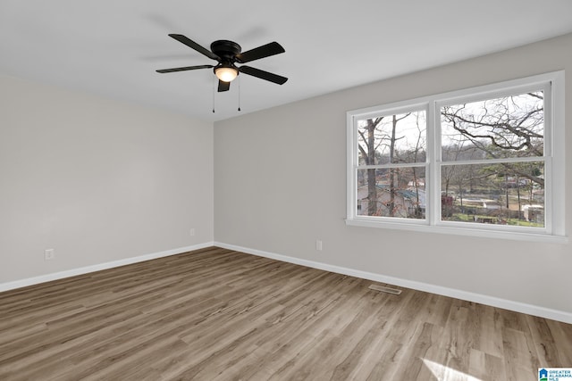 empty room featuring a ceiling fan, wood finished floors, visible vents, and baseboards