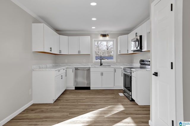 kitchen with appliances with stainless steel finishes, light wood-type flooring, crown molding, and a sink