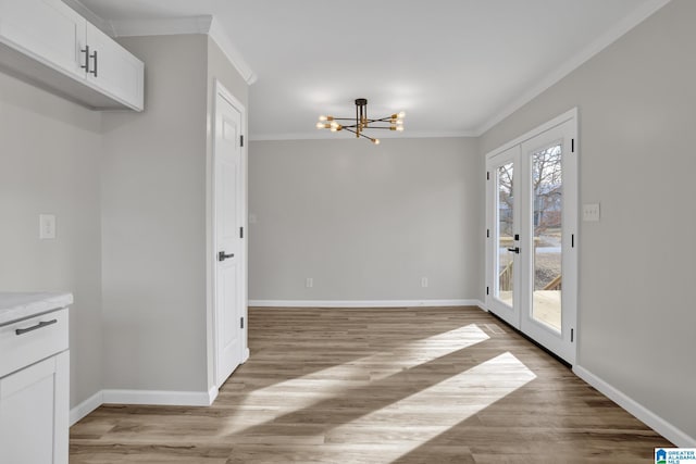 unfurnished dining area with a chandelier, ornamental molding, light wood-style flooring, and baseboards