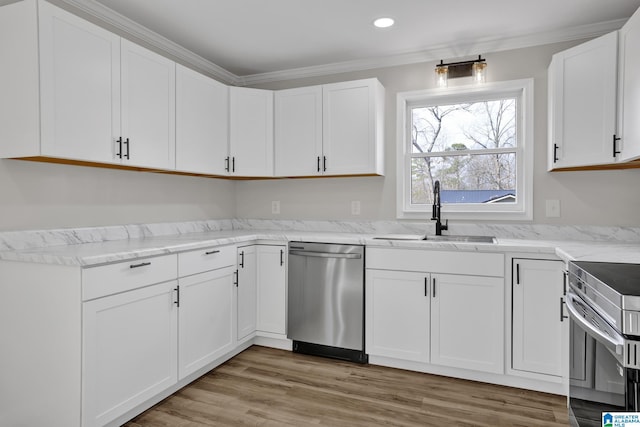 kitchen featuring light wood finished floors, white cabinets, stainless steel appliances, crown molding, and a sink