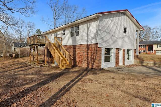 back of house featuring stairs, dirt driveway, brick siding, and a wooden deck