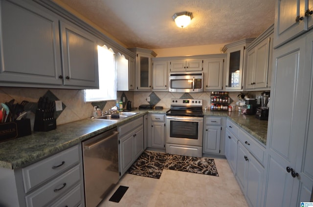 kitchen featuring glass insert cabinets, tasteful backsplash, appliances with stainless steel finishes, and gray cabinetry