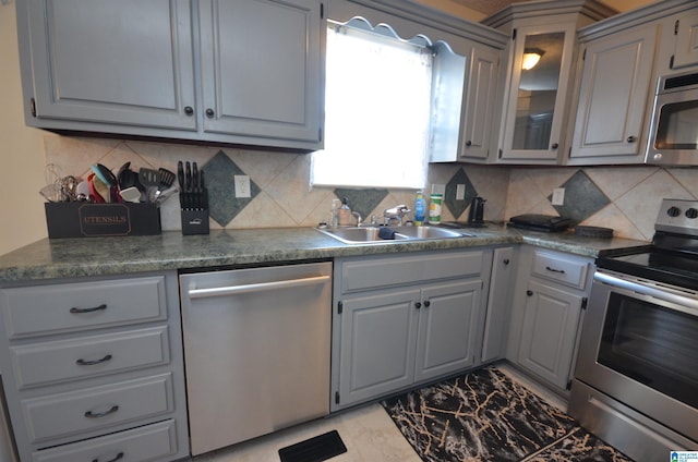 kitchen featuring tasteful backsplash, glass insert cabinets, appliances with stainless steel finishes, gray cabinetry, and a sink