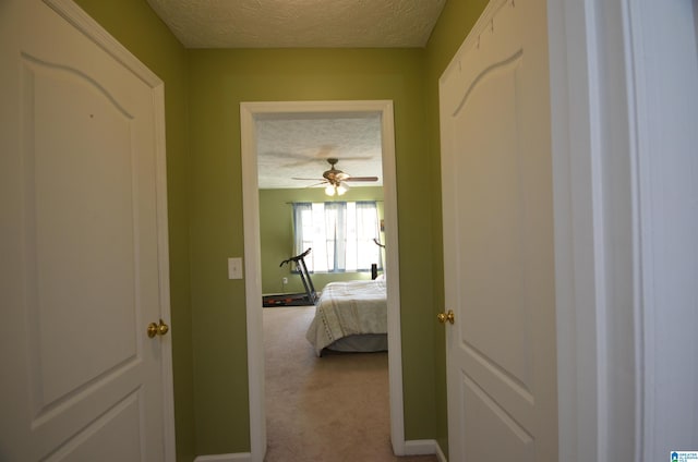 hallway with a textured ceiling, baseboards, and carpet flooring