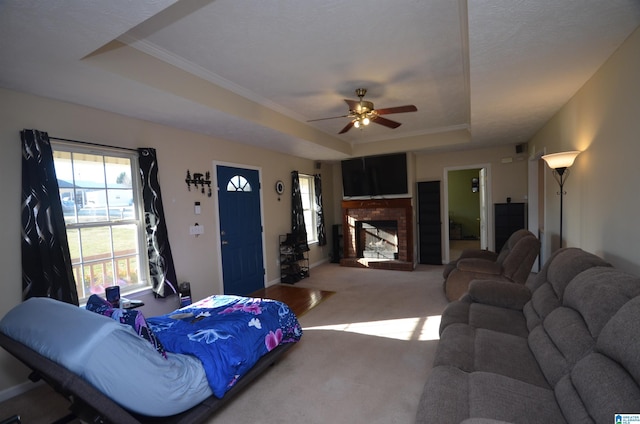 carpeted bedroom featuring a ceiling fan, a tray ceiling, a brick fireplace, and crown molding