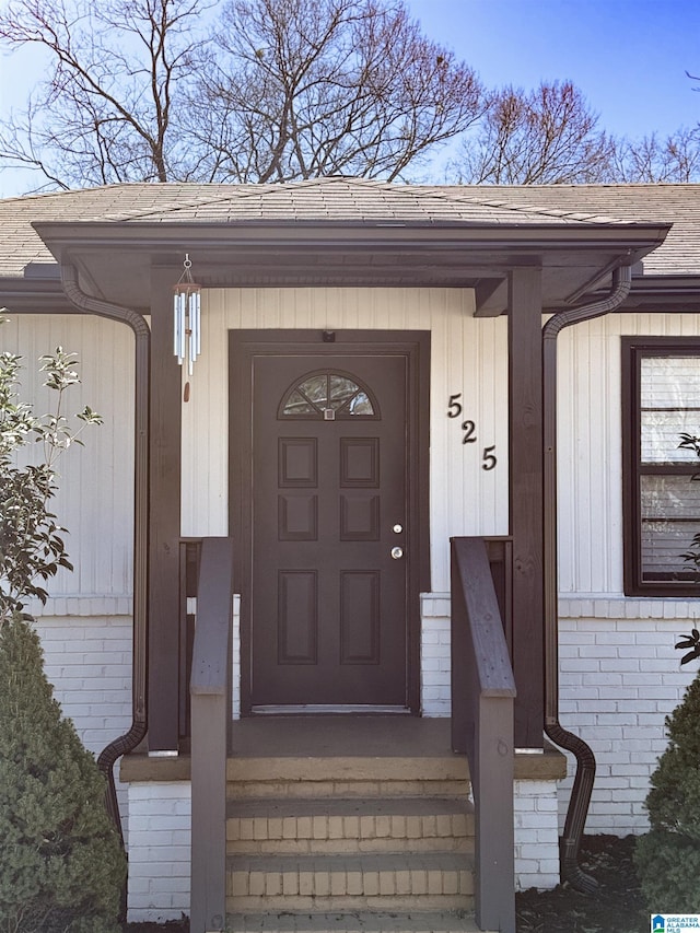 view of exterior entry with brick siding and roof with shingles