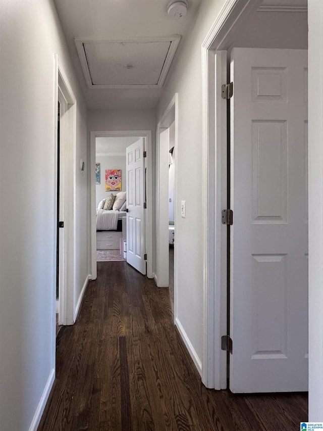 hallway with dark wood-style flooring, attic access, and baseboards