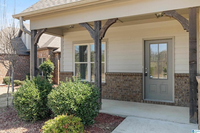 doorway to property featuring brick siding and a shingled roof