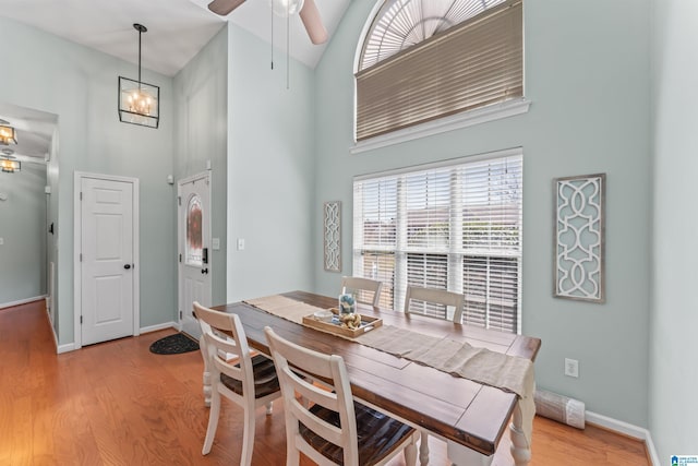 dining room with light wood finished floors, ceiling fan with notable chandelier, baseboards, and a towering ceiling