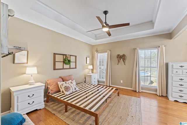 bedroom featuring crown molding, baseboards, light wood-style flooring, a raised ceiling, and a ceiling fan