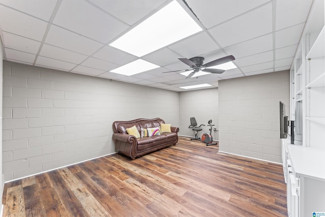 sitting room with a paneled ceiling, concrete block wall, ceiling fan, and wood finished floors