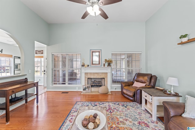 living room with a ceiling fan, wood finished floors, baseboards, and a tile fireplace