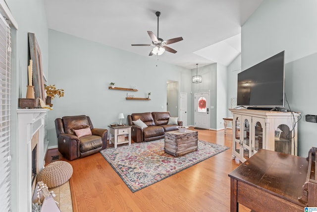 living area featuring a ceiling fan, wood finished floors, a fireplace, and vaulted ceiling